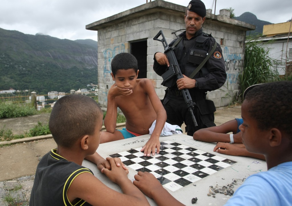 Crianças jogam dama no alto do morro observadas por um policial do Bope, armado com um fuzil - Foto: Marcia Foletto/Divulgação