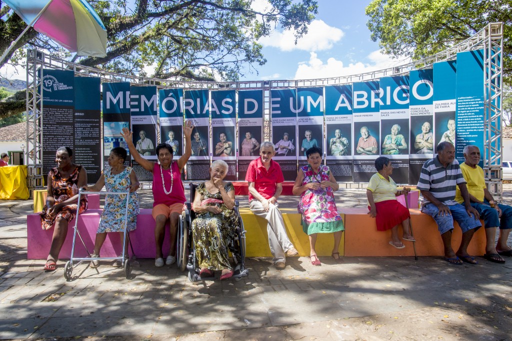 Idosos moradores do Abrigo Tiradentes que foram homenageados com uma exposição pela Mostra Valores posam em frente a seus retratos na praça principal da cidade - Foto: Leo Lara/Universo Produção/Divulgação