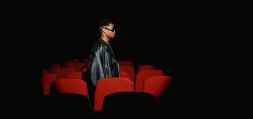 man black leather jacket standing behind red theatre seat